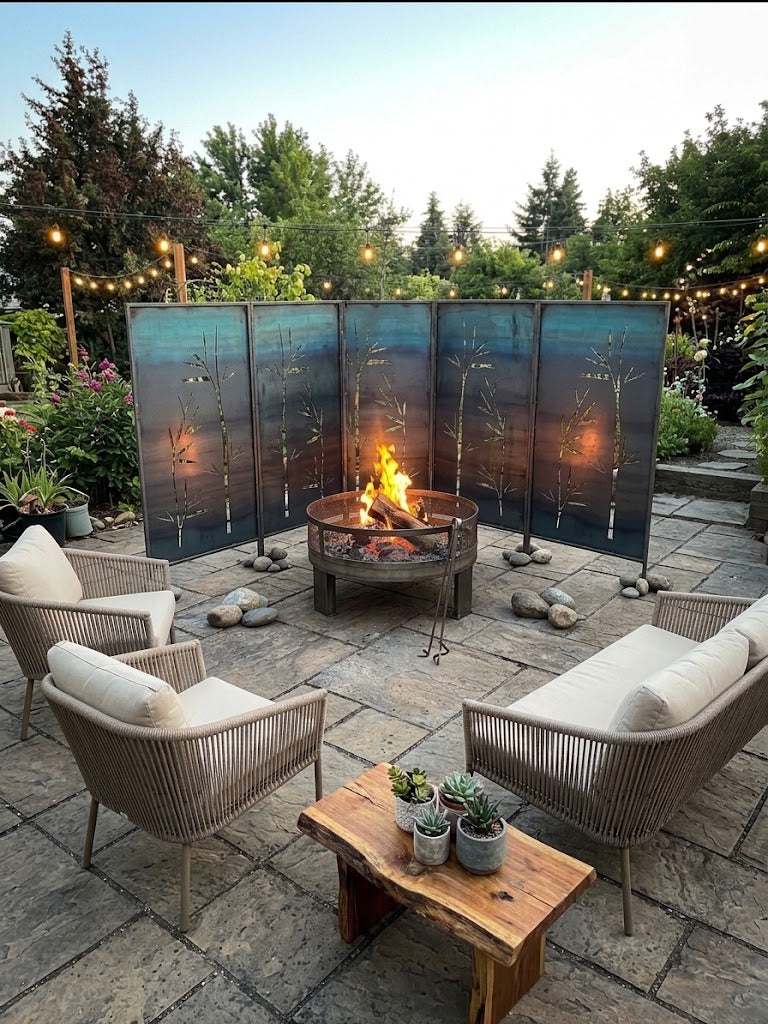Five Ironman Bamboo Grove steel privacy screens arranged in a semi-circle around a copper fire pit on a stone paver patio in the evening, with rope patio seating, a live-edge wood coffee table with potted succulents, and string lights overhead, showing how multiple two-packs can be combined to create a wider continuous privacy screen for outdoor entertaining