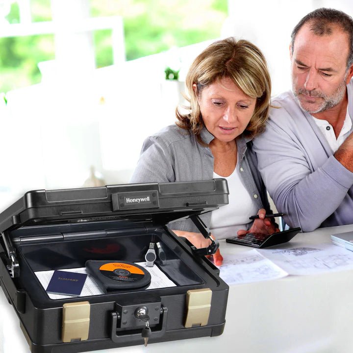 Two people looking into a black Honeywell safe box on a table.