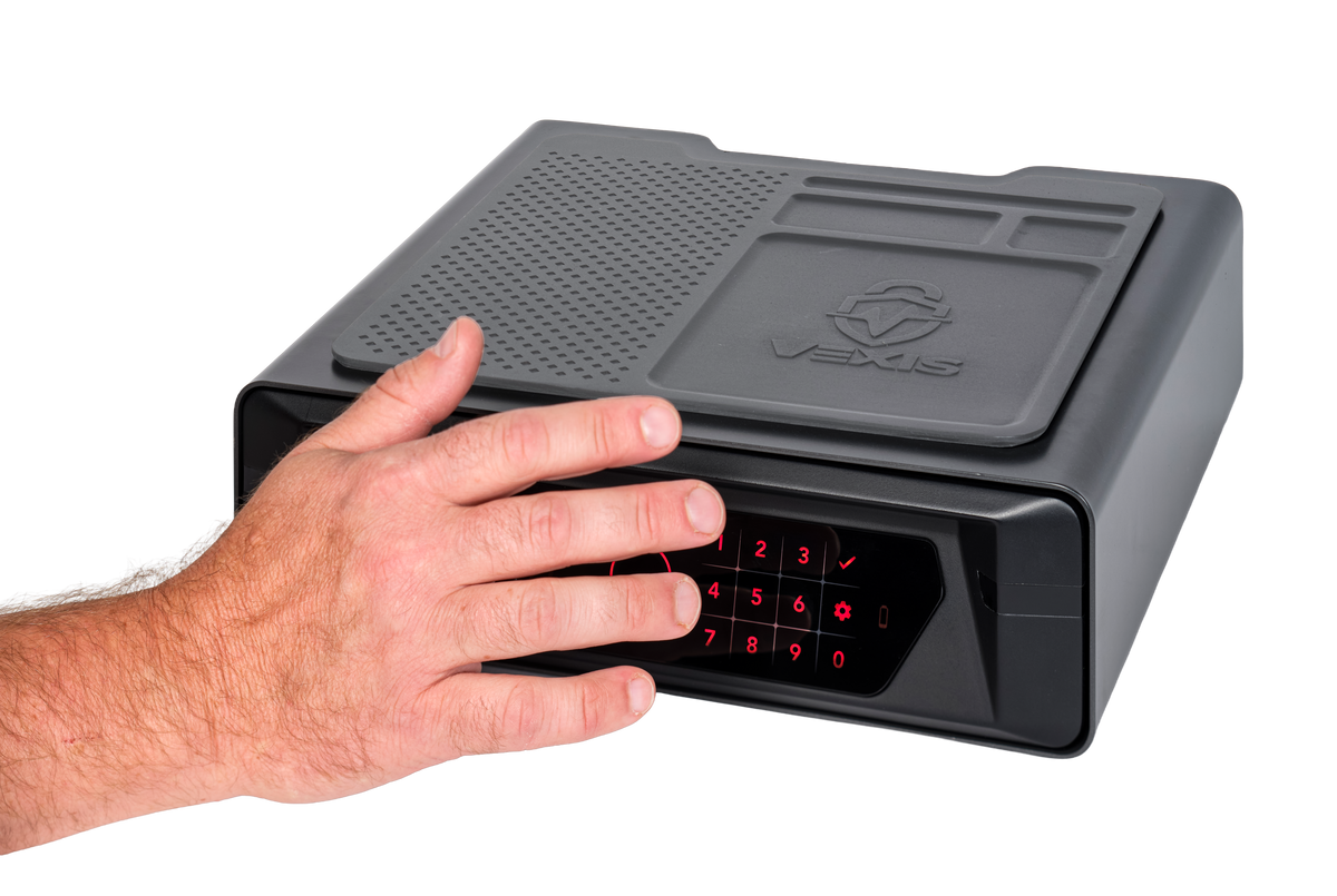 Person's open hand hovering above the Hornady VEXIS Night Guard bedside safe with palm positioned over the circular palm vein biometric scanner on the front, demonstrating contactless palm vein recognition for fast bedside access, dark gray safe with rubberized organizer mat and VEXIS logo on top