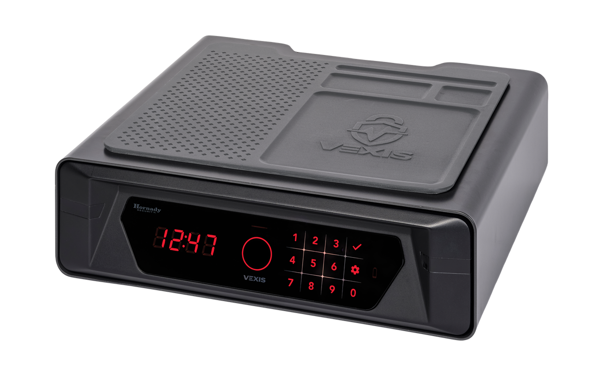 Hornady VEXIS Night Guard palm vein bedside safe in dark gray with red LED clock display showing 12:47, red-lit VEXIS touch keypad with circular palm vein biometric scanner, Hornady Security branding on the front, and top surface featuring a rubberized non-slip organizer mat with phone stand groove and embossed VEXIS logo, angled front view