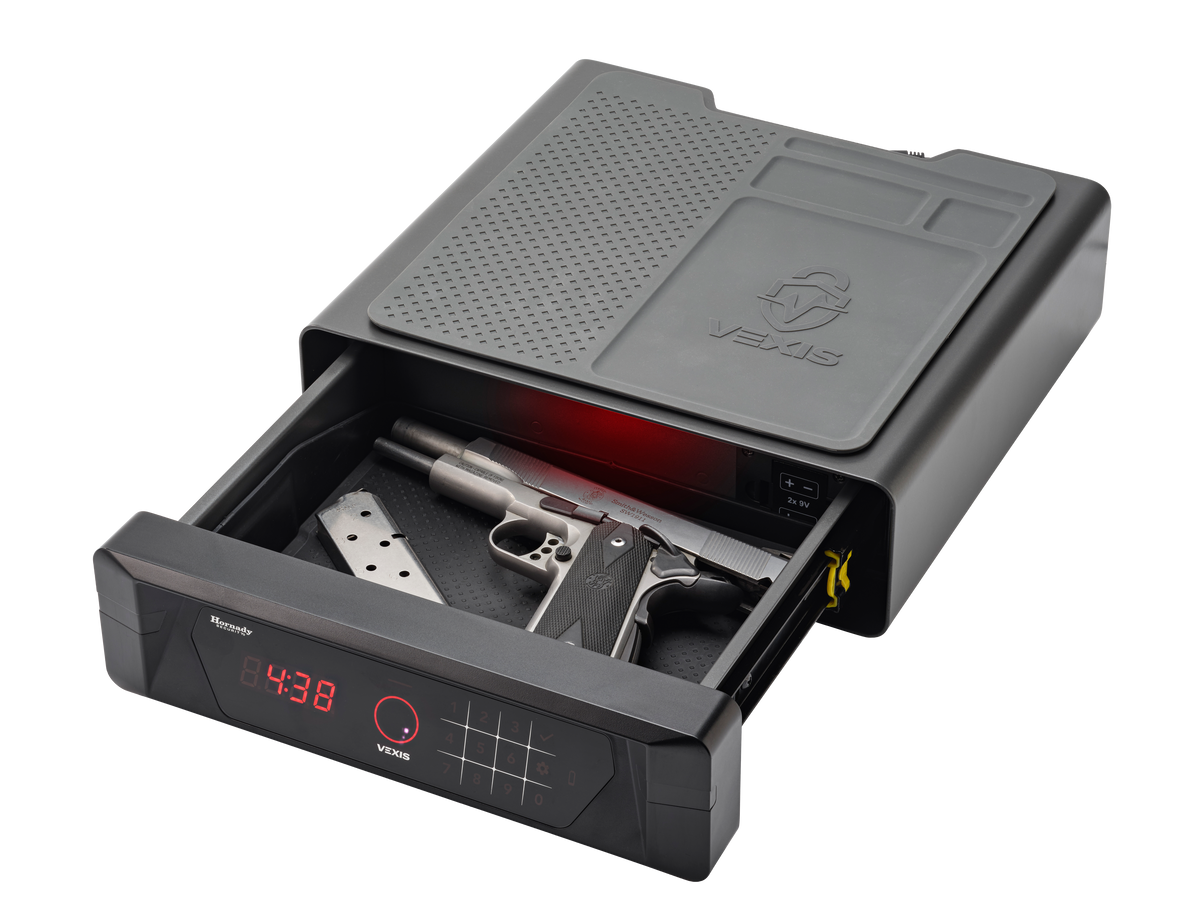 Hornady VEXIS Night Guard bedside safe with the sliding drawer fully extended showing a stainless steel Smith & Wesson SW1911 pistol with a spare magazine stored inside on the padded interior, VEXIS keypad and palm vein scanner illuminated in red on the front panel with LED clock showing 4:38, two 9V battery compartment visible on the interior right wall, and VEXIS logo embossed on the top surface