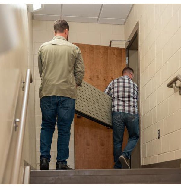Two men carrying a disassembled panel of the Hornady VEXIS Mobilis safe up a stairwell to show modular portability