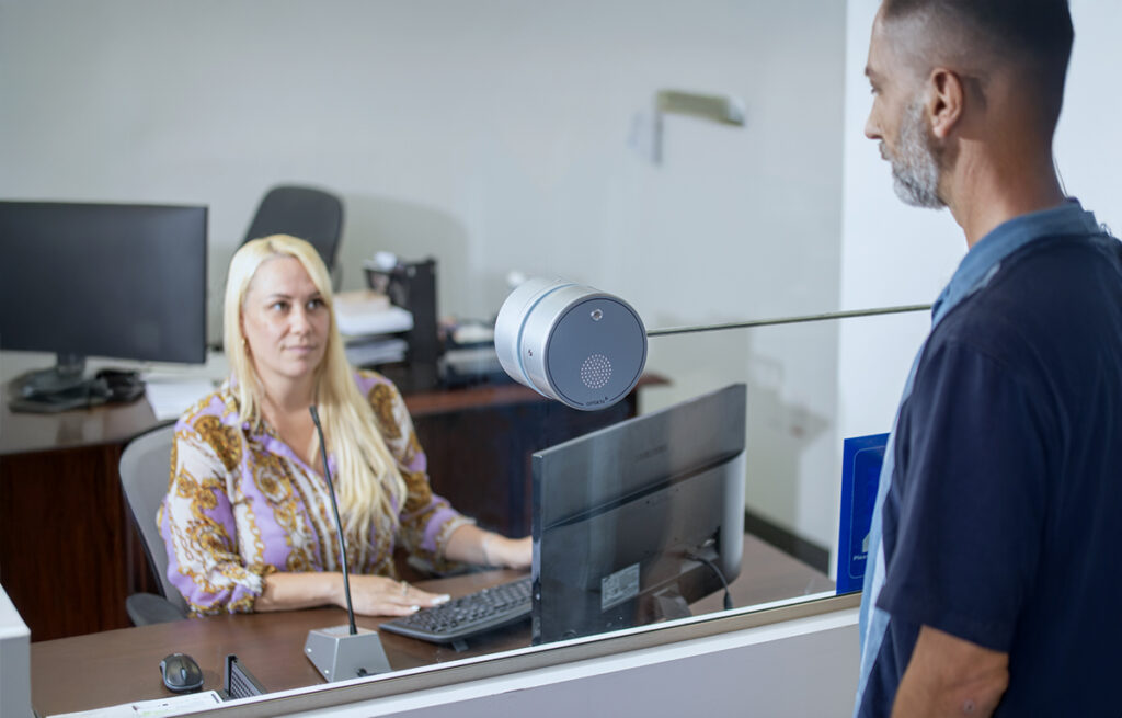 Contacta STS-K021 all-in-one intercom puck between a staff member and customer at a service counter security glass