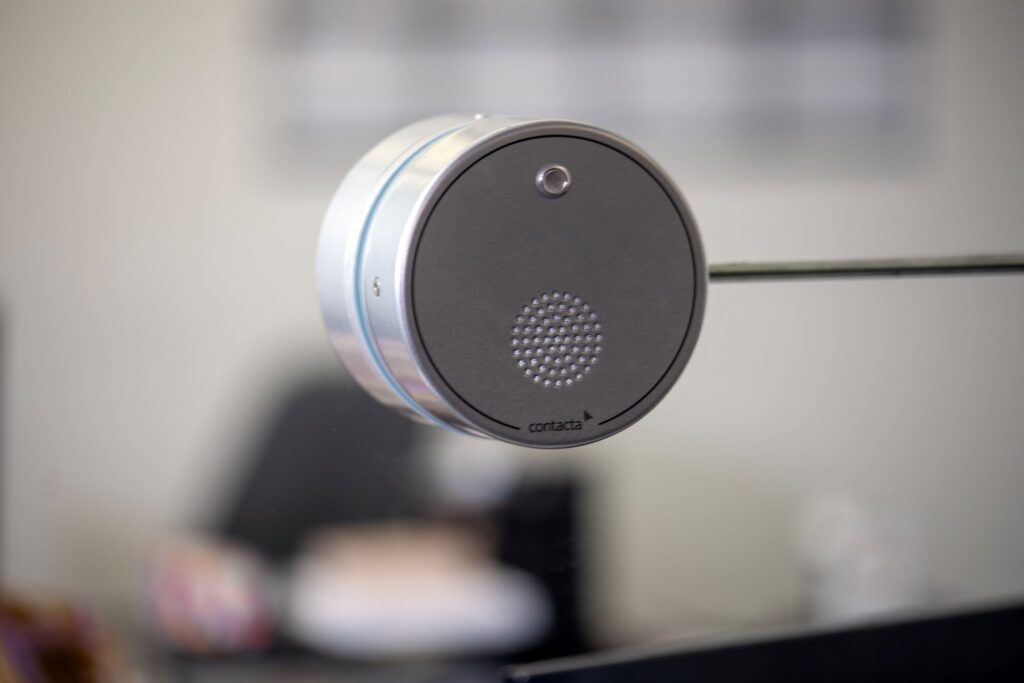 Close-up of the Contacta all-in-one glass-mounted speaker and microphone puck with chrome bezel and speaker grille