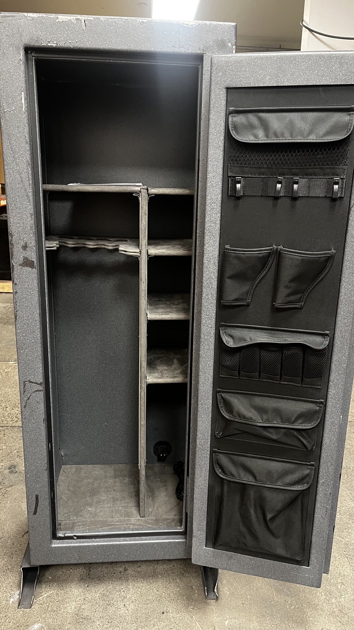 View of the inside of the safe. It comes with a power out on the bottom right corner. The safe also has a few adjustable shelfs. The door has two pistol holders and zipper organizers. 