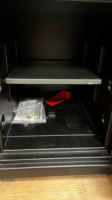 Close-up of the inside of the safe. The shelf has a small paint chip on the lower right edge. The shelf is adjustable, and it does come with a bolt down hole in the center of the safe. It also has two extra shelf clips. 