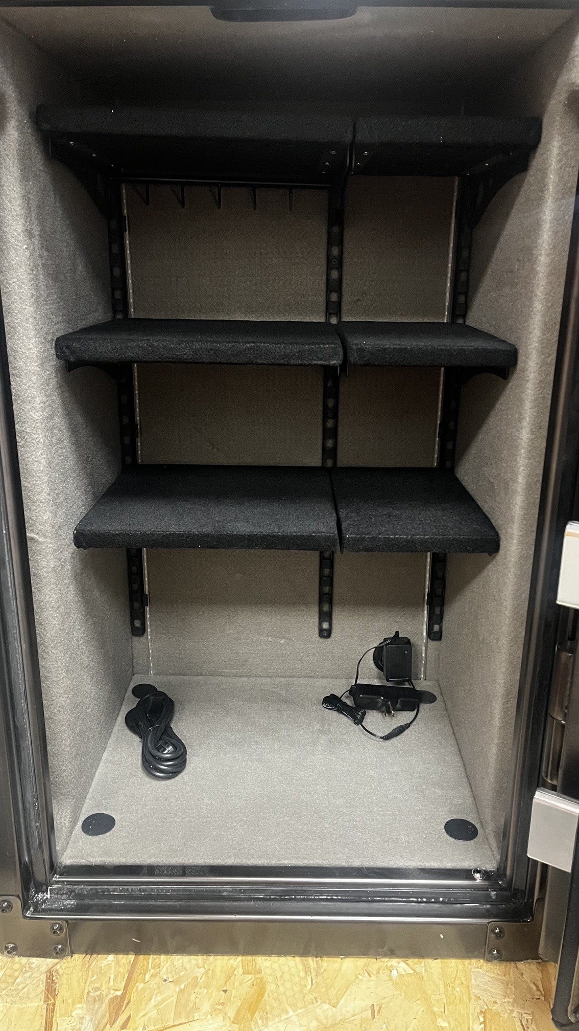 Close-up view of the inside of the safe. It has 4 predrilled holes to bolt it down. Six adjustable shelves and a power outlet on the bottom right of the safe. 