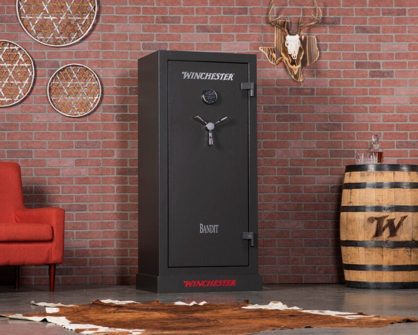 Winchester Bandit 19 slate gun safe styled in a brick-wall den with red chair, Winchester barrel keg, and deer skull mount