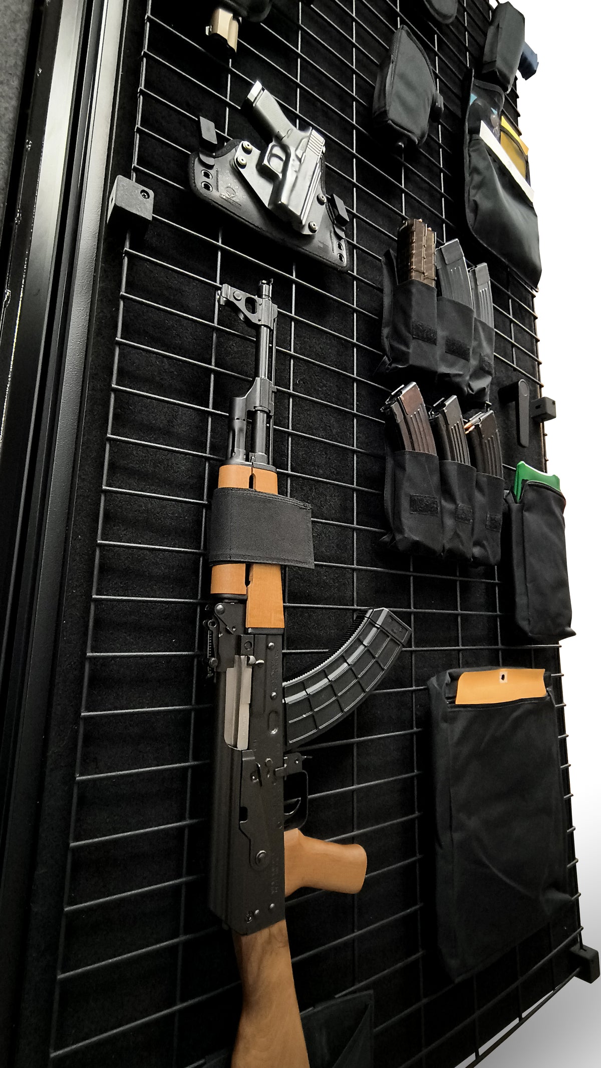 Wall-mounted gun rack with various firearms and accessories on a black grid background