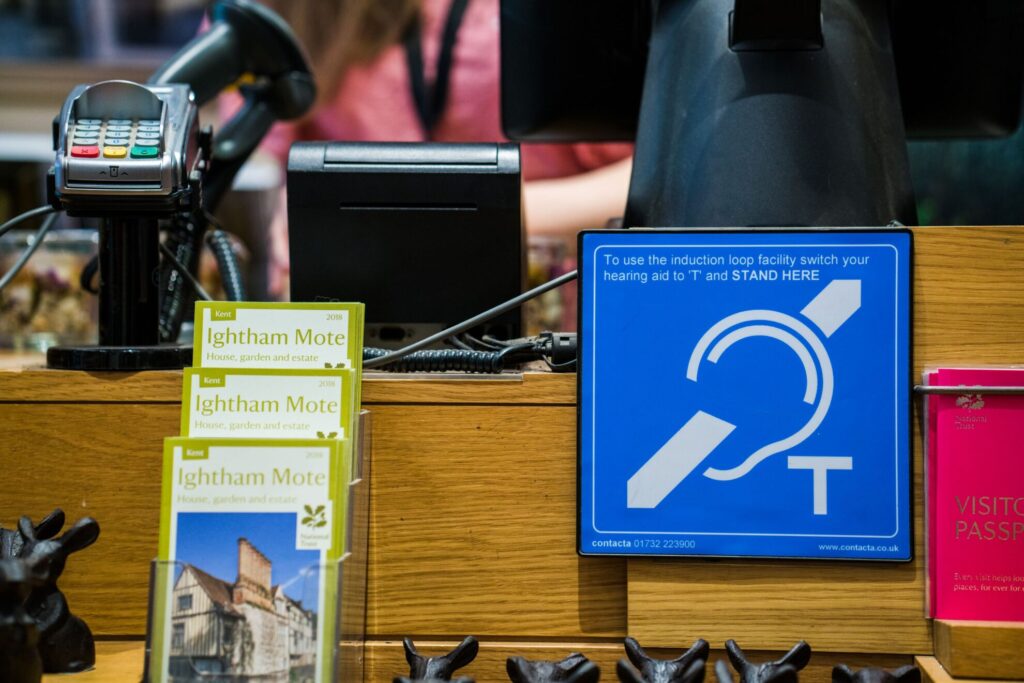 Close-up of the Contacta IL-AE97 hearing loop aerial on a museum shop counter with pamphlets and a payment terminal