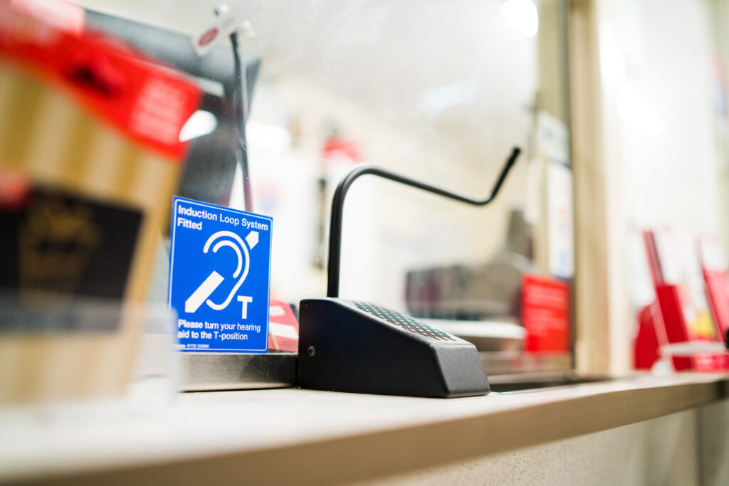 Contacta STS-K035 Black Textured half-bridge bar customer microphone installed at a retail counter with hearing loop signage