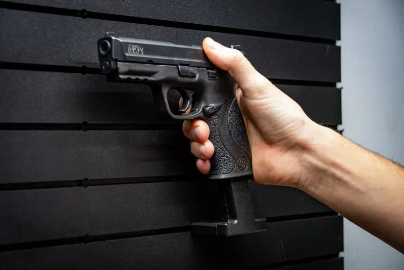 Hand holding a black handgun against a dark slat wall