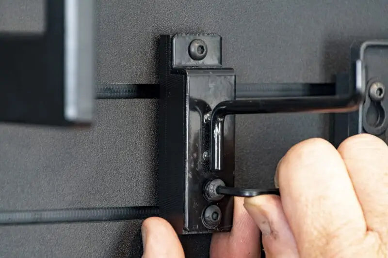 Hand adjusting a black metal bracket on a gray wall.