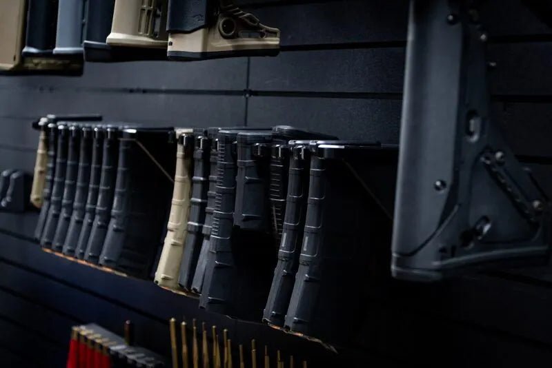 Wall-mounted gun rack with various firearms and accessories on a dark background