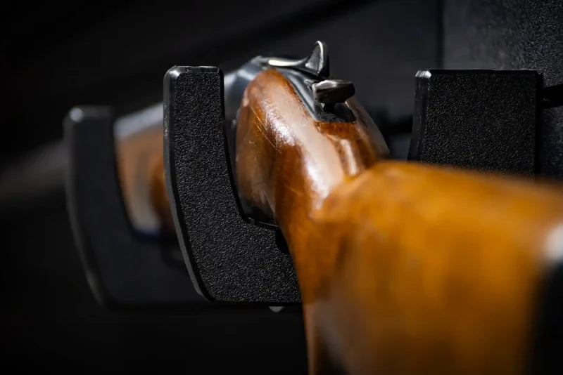Close-up of a Tactical Walls MWHRACKRS ModWall rack cradling a wooden rifle stock, showing the black HDPE hook design that supports the firearm while protecting the finish