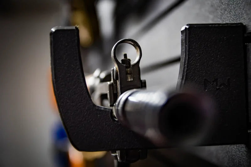 Close-up of a Tactical Walls MWHRACKRS ModWall rack cradling a rifle barrel with the front sight post visible, showing the black HDPE rack profile with subtle MW branding on the side