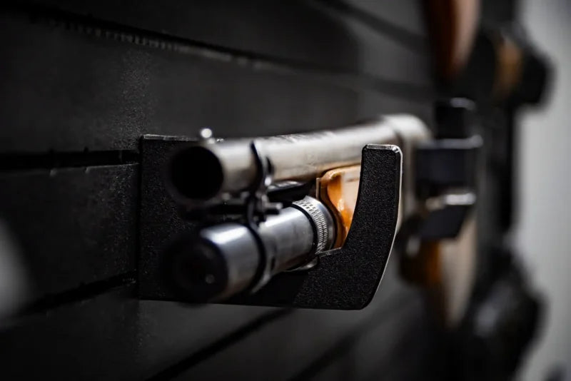 Close-up of a Tactical Walls MWHRACKRS ModWall rack holding the receiver of a shotgun, showing the rack's black HDPE curved profile that safely supports metal barrel and receiver components