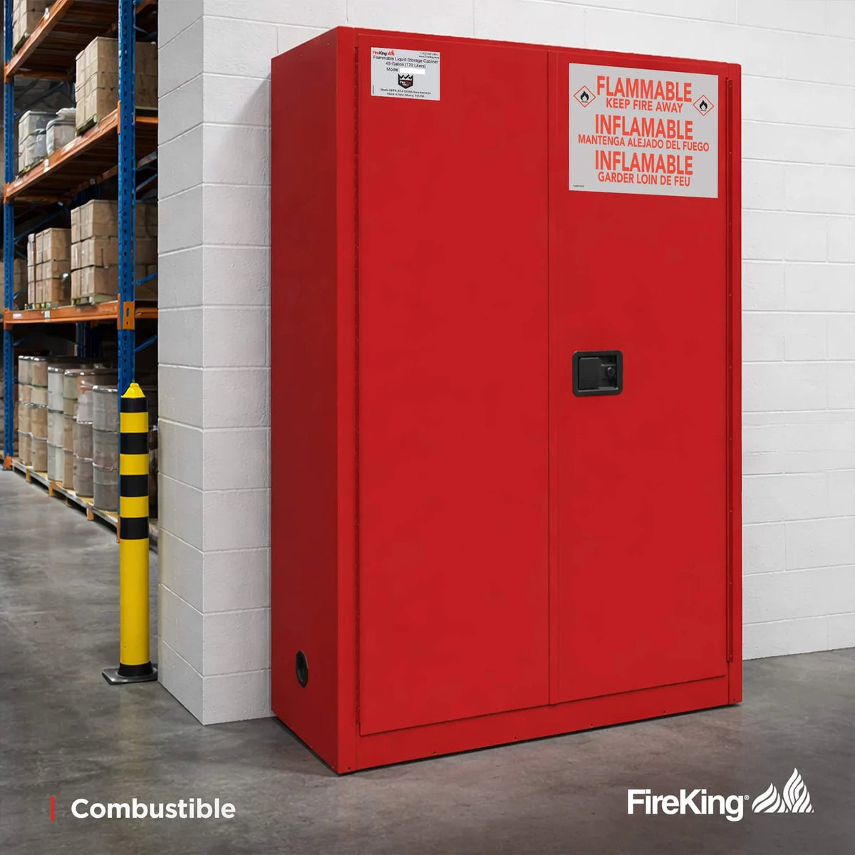 FireKing SC45 45-gallon flammable safety cabinet in red installed in a warehouse setting for combustible liquid storage, positioned against a painted cinderblock wall with pallet racking of drums and inventory boxes visible in the background and a yellow-and-black safety bollard nearby