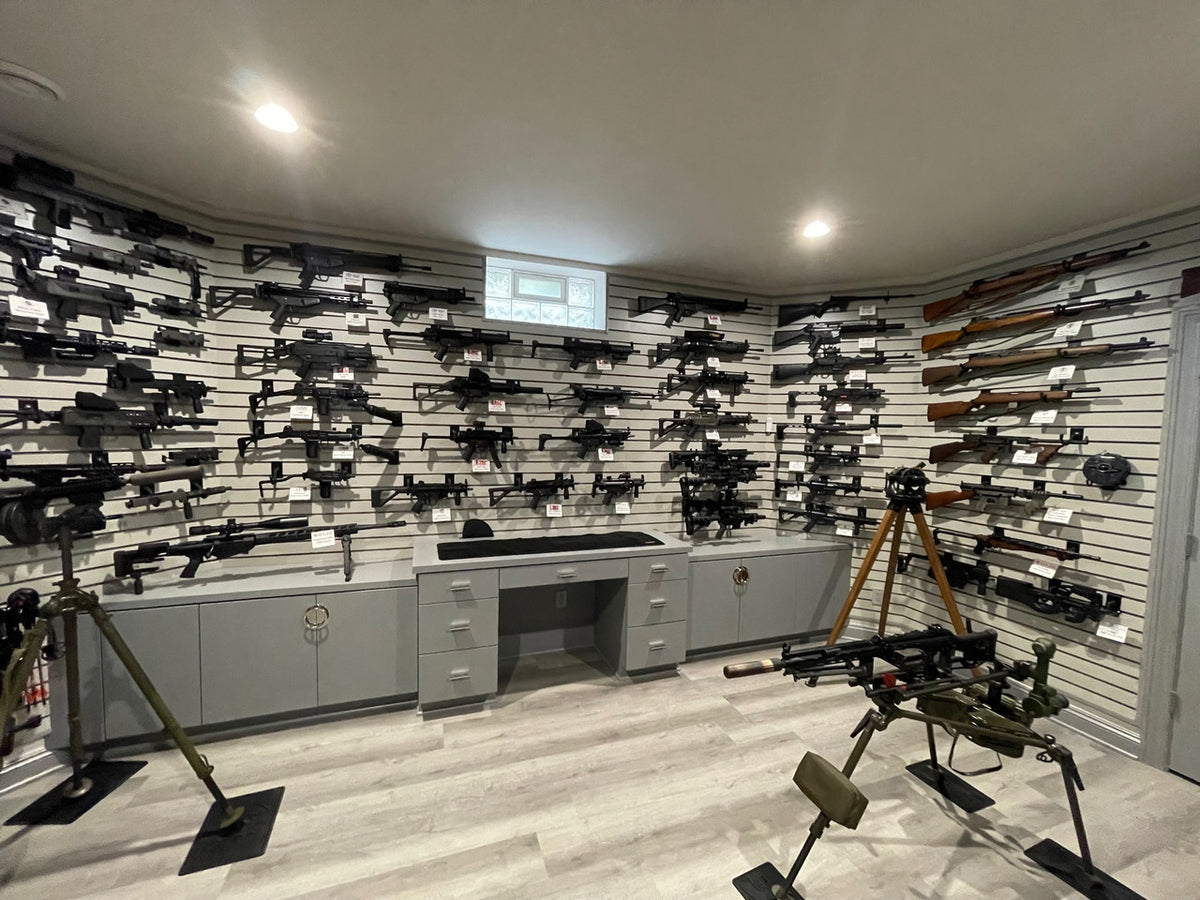 Room with walls lined with various firearms and a central desk.