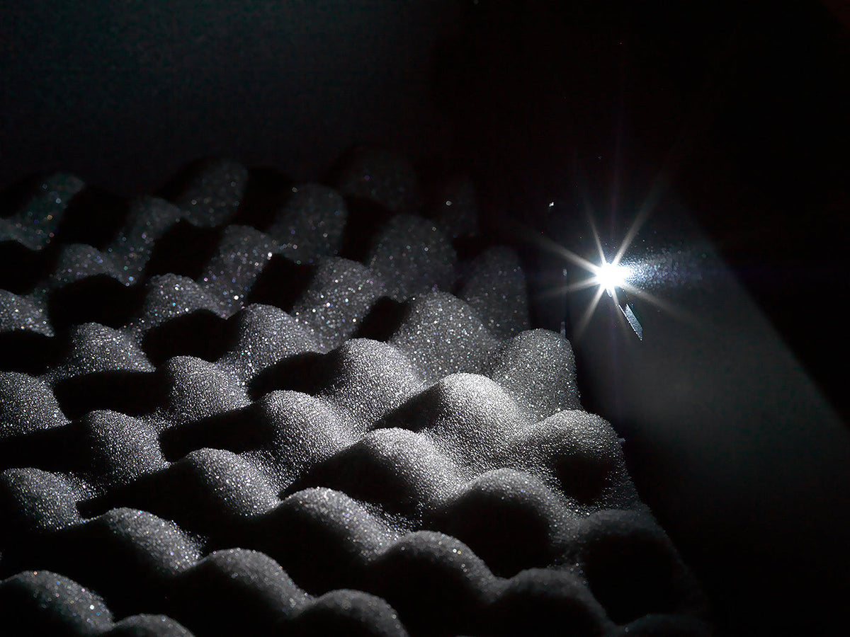 Black acoustic foam panel with a bright light source on a dark background