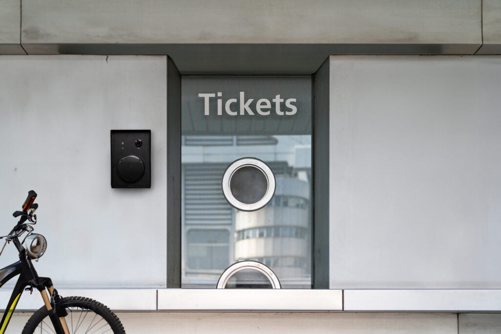 K009-IP outdoor call unit mounted on a concrete wall beside an outdoor ticket service window in an urban setting