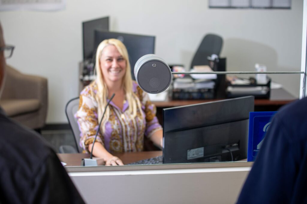 Contacta STS-K021 all-in-one puck installed at a service counter security glass with a staff member visible behind
