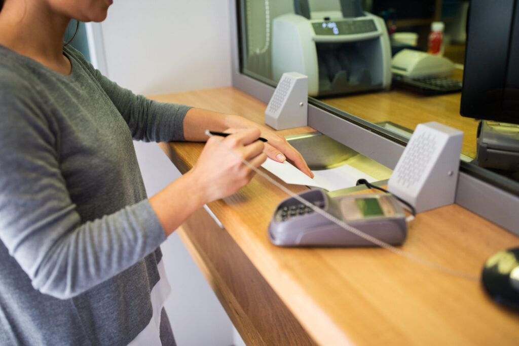 Customer at a bank counter using the Contacta STS-K002 surface-mounted speaker and microphone through glass
