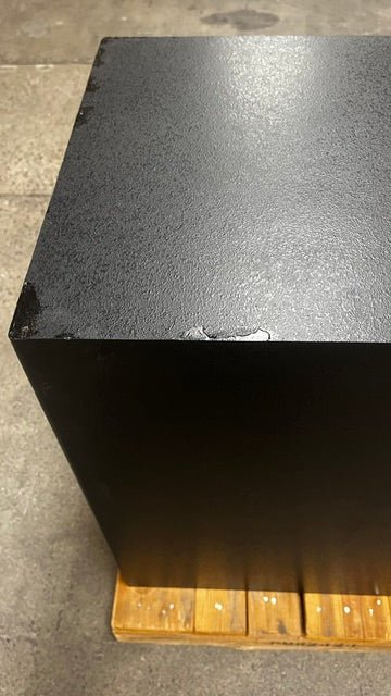 View of the top left side of the safe. It has a paint chip. It has been painted in black to match the color of the safe. 