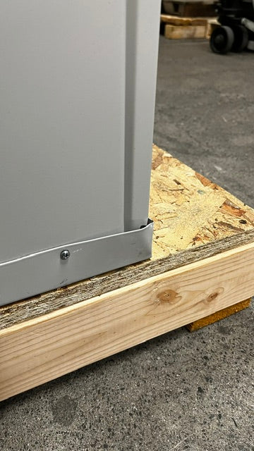 View of the lower back right side of the file cabinet. It has a small dent on the edge. 