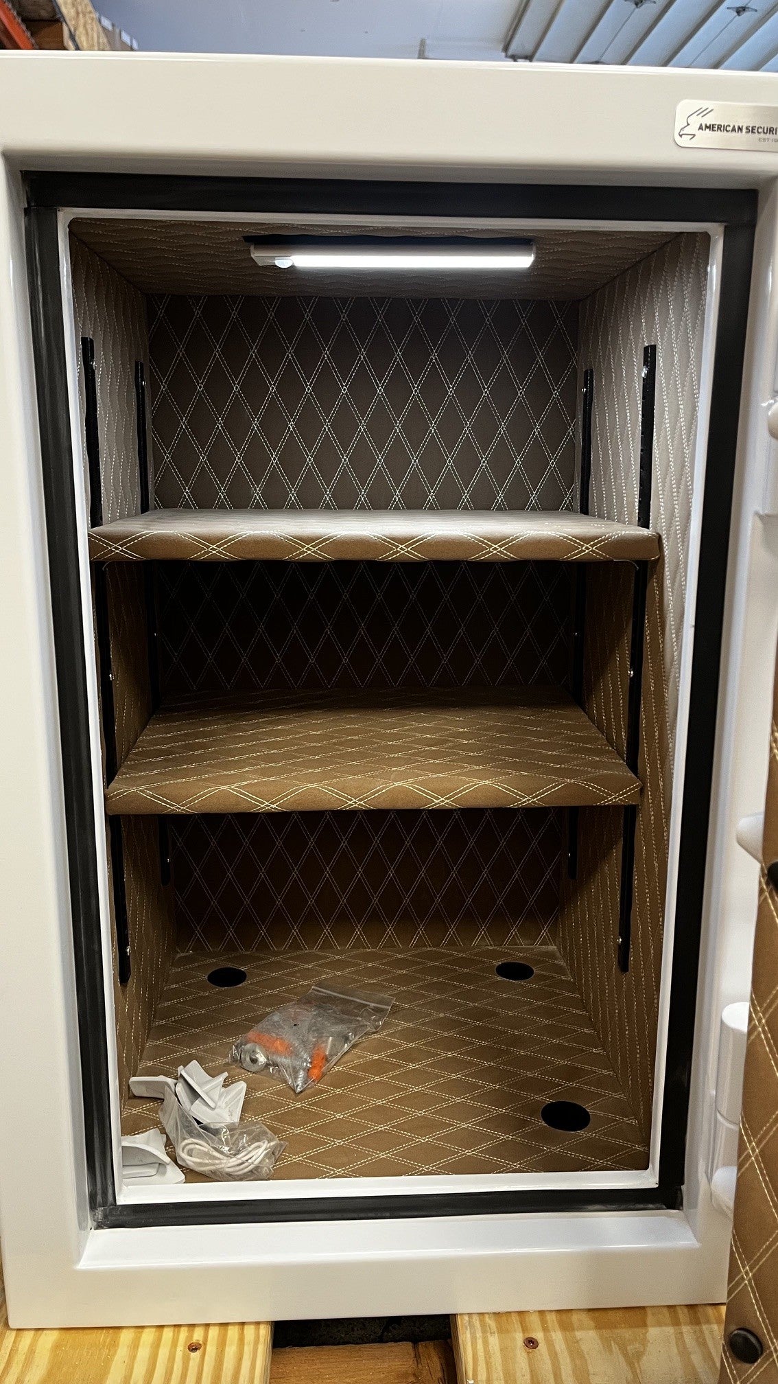 Close up view of the inside of the safe. It has two adjustable shelves, and it comes with an LED light kit. It has four predrilled holes to be mounted to the floor. 