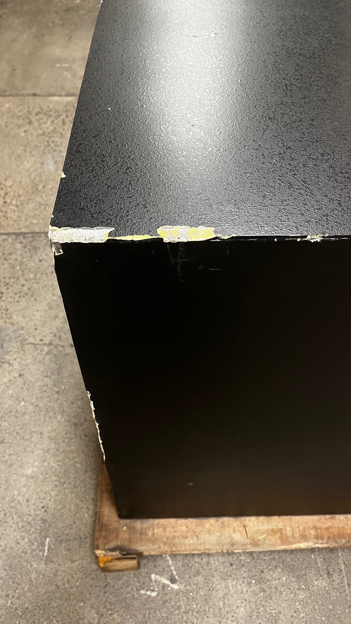 Close-up view of the top left corner on the back of the safe. It has chips on the corner and along the edge. 