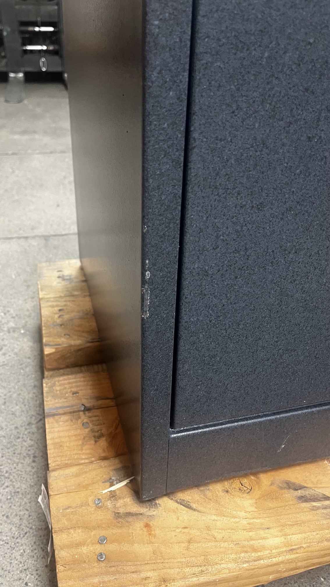 View of a left side of the safe where it has a chip on the paint. The chip on the paint is alongside the edge of the safe. 