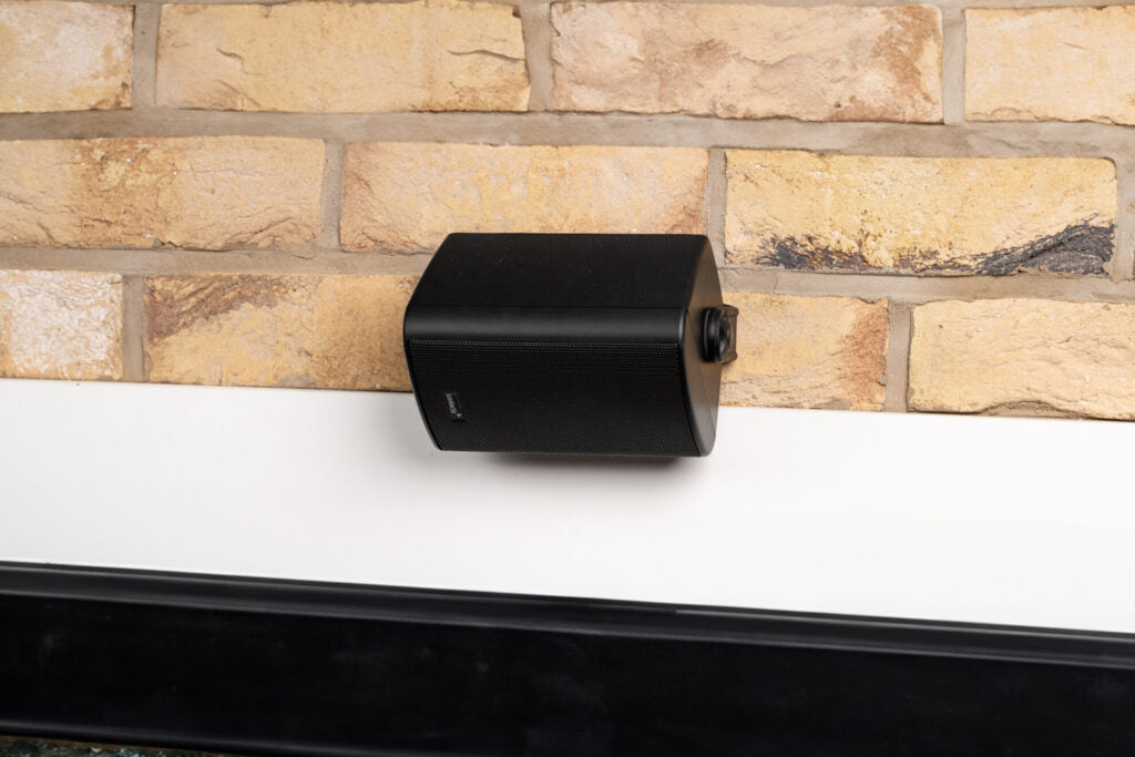 Close-up of the Contacta STS-S80-IP IP54 outdoor speaker mounted on a tan brick wall above a white counter ledge