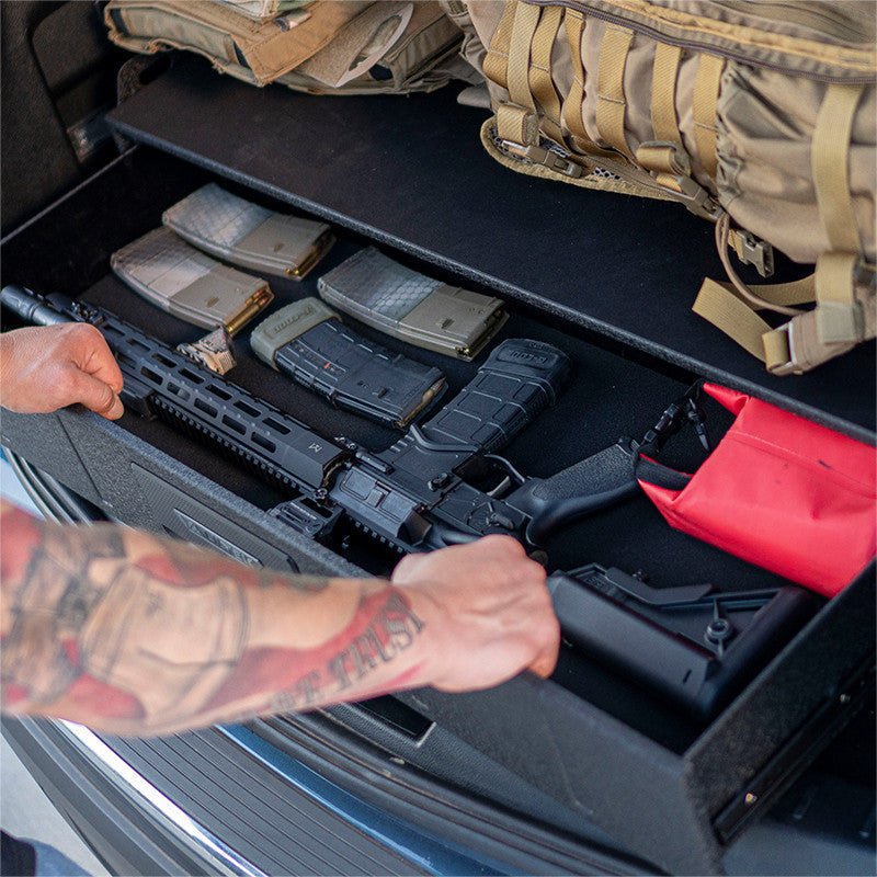 Hand pulling an AR rifle from the open Vaultek SLV200i drawer in a vehicle with loaded AR magazines stored alongside