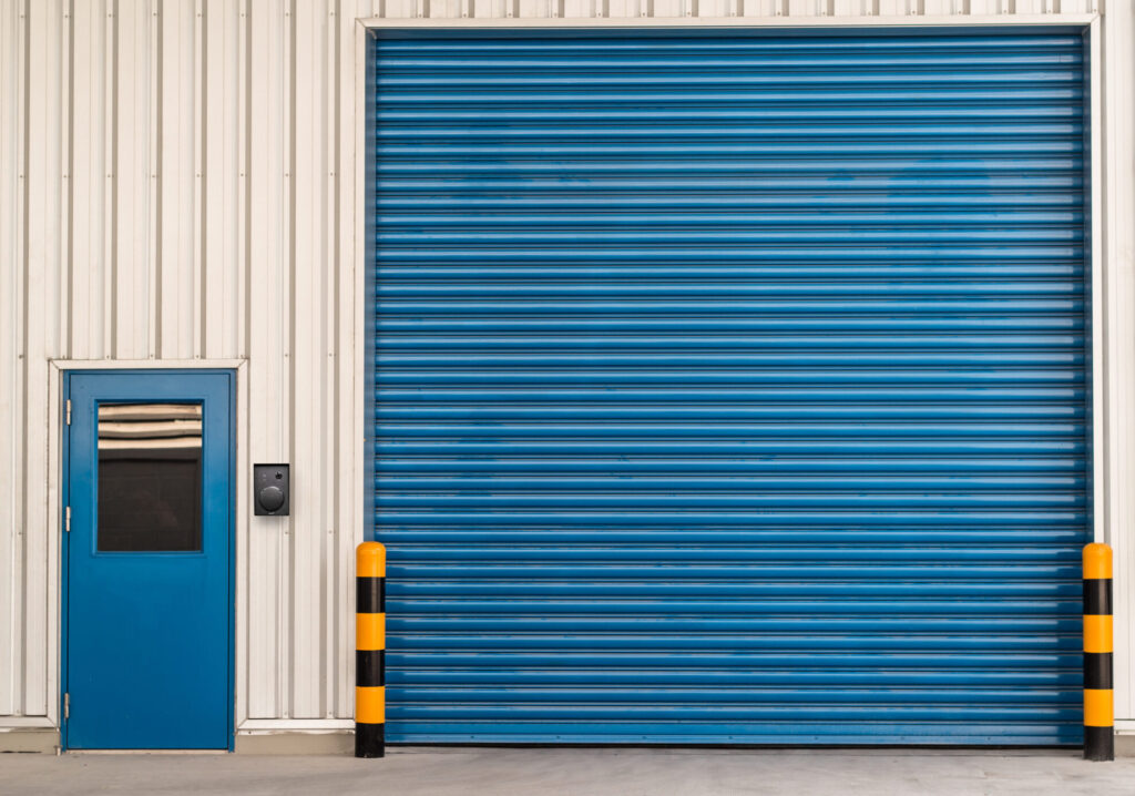 Contacta K009-IP outdoor call unit mounted at a warehouse entry door beside a blue roll-up loading dock door